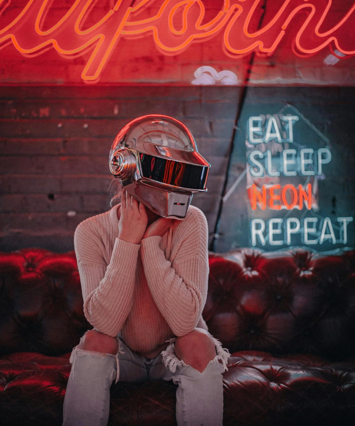A figure in a chrome helmet under neon signs
